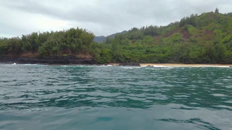 4K-Hawaii-Kauai-Boating-on-ocean-floating-right-to-left-from-beach-to-waves-crashing-on-rocky-shoreline-to-reveal-more-shoreline-in-cloudy-distance