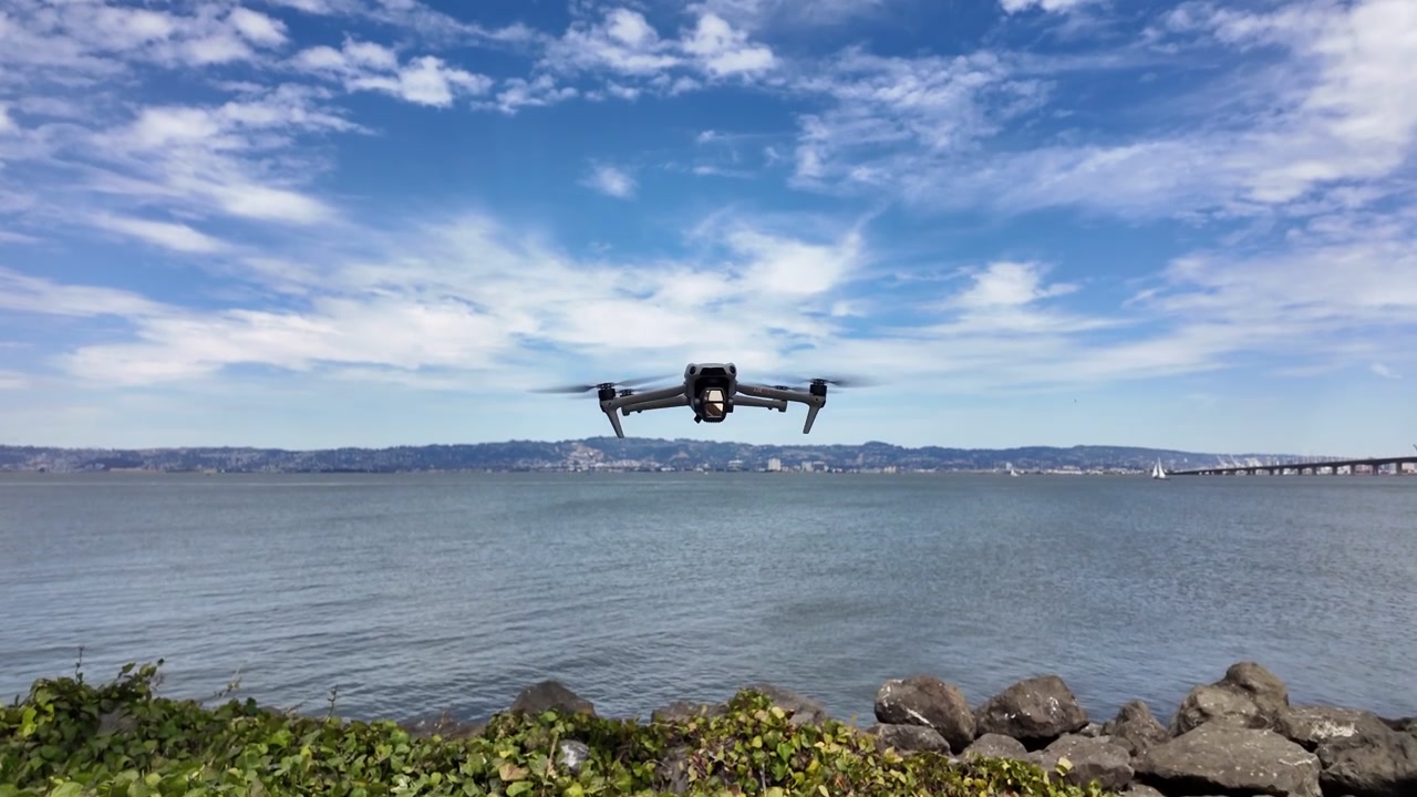 Forbrugerdrone flyver dynamisk over Treasure Island, San Francisco Bay, med levende blå himmel, teksturerede skyer og bybillede. Klart dagslys, jævn bevægelse og naturskønne luftoptagelser.