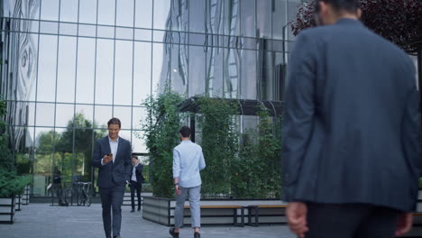 gente corporativa caminando por el patio del centro de negocios con trajes. exterior de vidrio moderno.