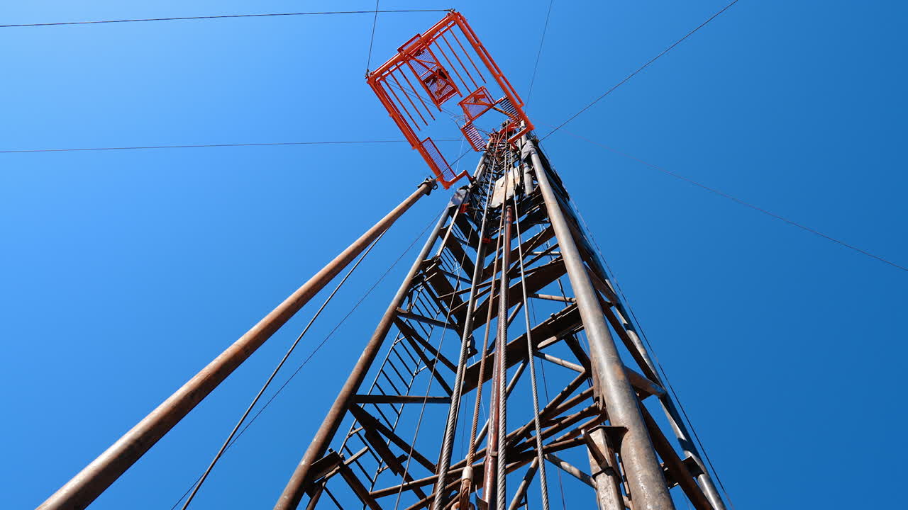 Looking up at the tower for natural resources boring. Low angle view at the derrick for drilling oil. Blue clear sky at backdrop.