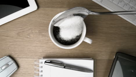 azúcar en cucharadita cayendo en una taza de café en un escritorio