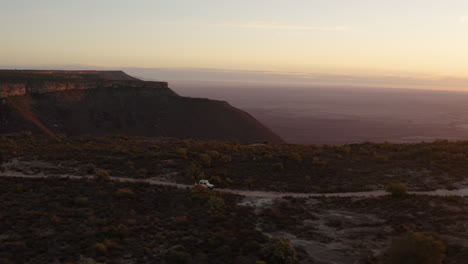 Wide-Drone-shot-Following-a-Land-Rover-Explorer-Driving-next-to-a-Mountain-Cliff-during-Sunset-in-the-Northern-Cape-of-South-Africa