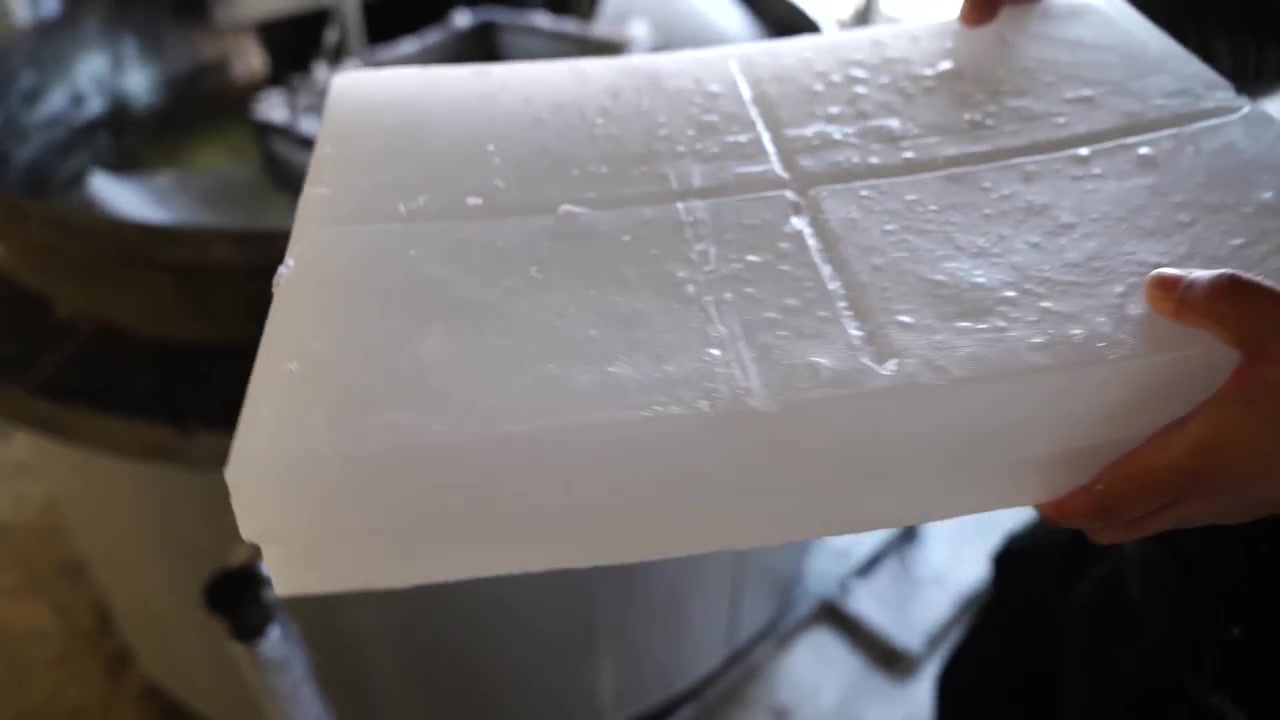 Operaio che solleva un grande blocco solidificato di cera bianca da una vasca di raffreddamento ad acqua in una fabbrica di candele giapponese.