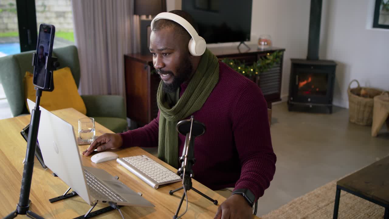 African American man clicking laptop tapping tablet waving for call using microphone in home office