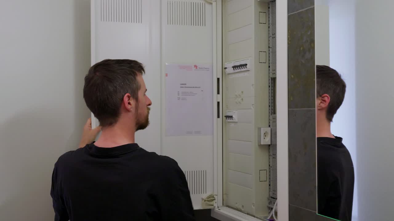 A person walks to an electrical cabinet, opens the door, switches a breaker on, closes the cabinet, and walks away