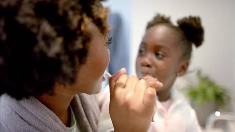 Happy-african-american-mother-and-daughter-brushing-teeth-in-bathroom,-slow-motion