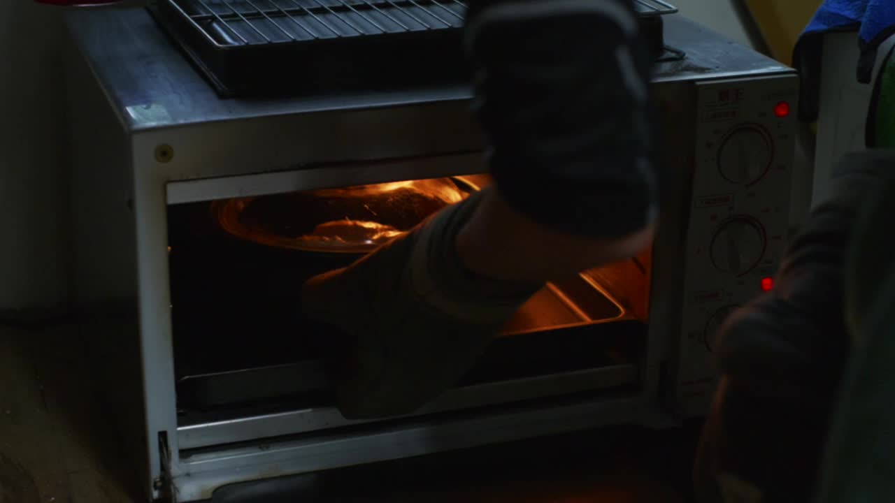 Assadeira com tampa sendo empurrada para dentro do forno e fechada, filmada em plano médio-detalhe em câmera lenta.