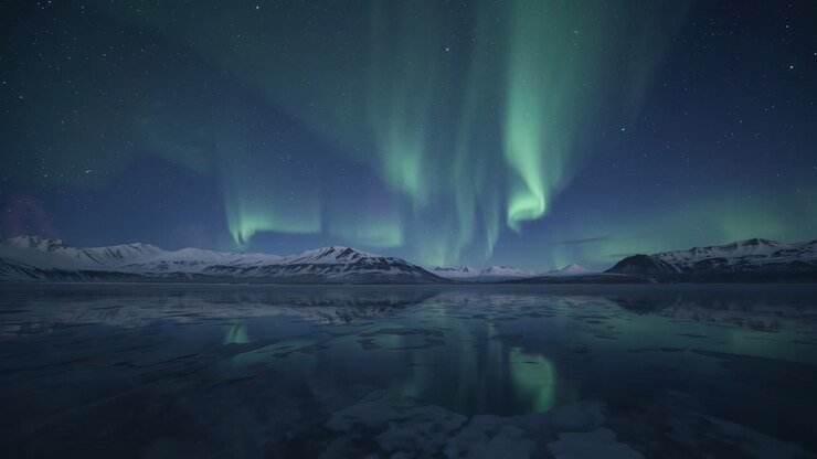 Emerging faint green glow initiating aurora borealis waving over frozen lake, beneath snowy peaks