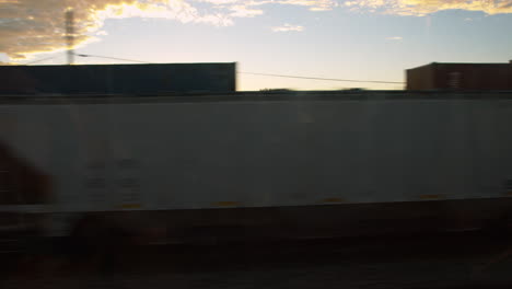 a view from a dirty train window of a sunset as a train passes other train cars.