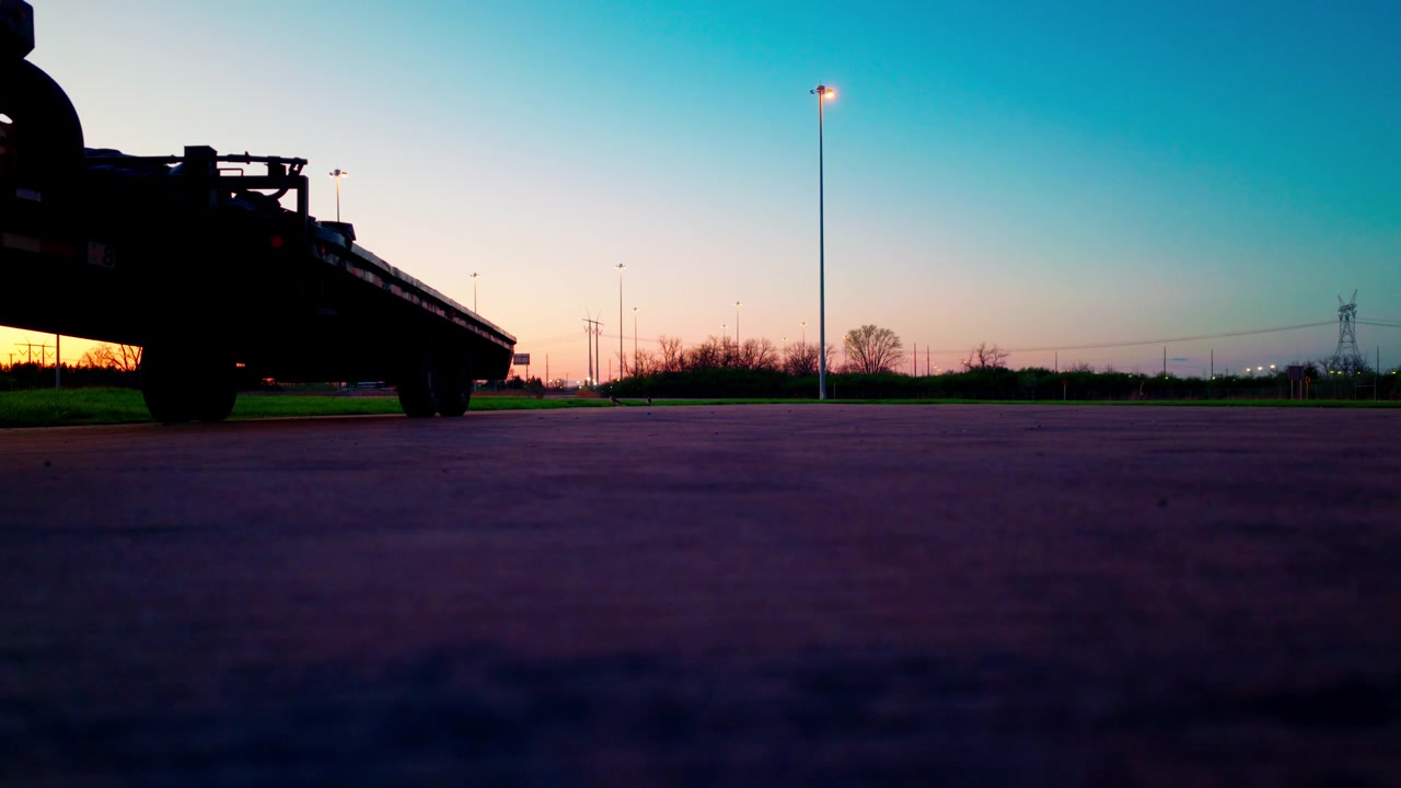 Rimorchio pianale commerciale per trasporto urgente parcheggiato al tramonto, che illustra le attività indipendenti di autotrasporto hotshot, la logistica del trasporto merci e la spina dorsale delle catene di approvvigionamento B2B.