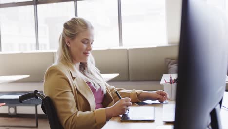 Happy-caucasian-casual-businesswoman-in-wheelchair-using-tablet-in-office,-in-slow-motion