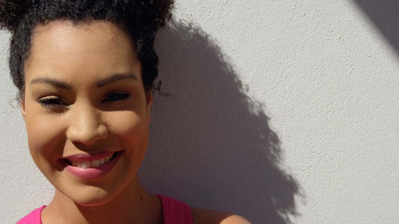 vista frontal de una joven mujer de raza mixta apoyada contra la pared en el patio trasero de la casa 4k