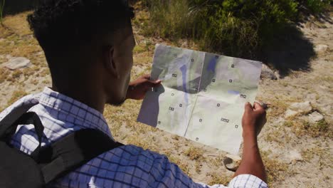African american man hiking reading a map in coastal countryside
