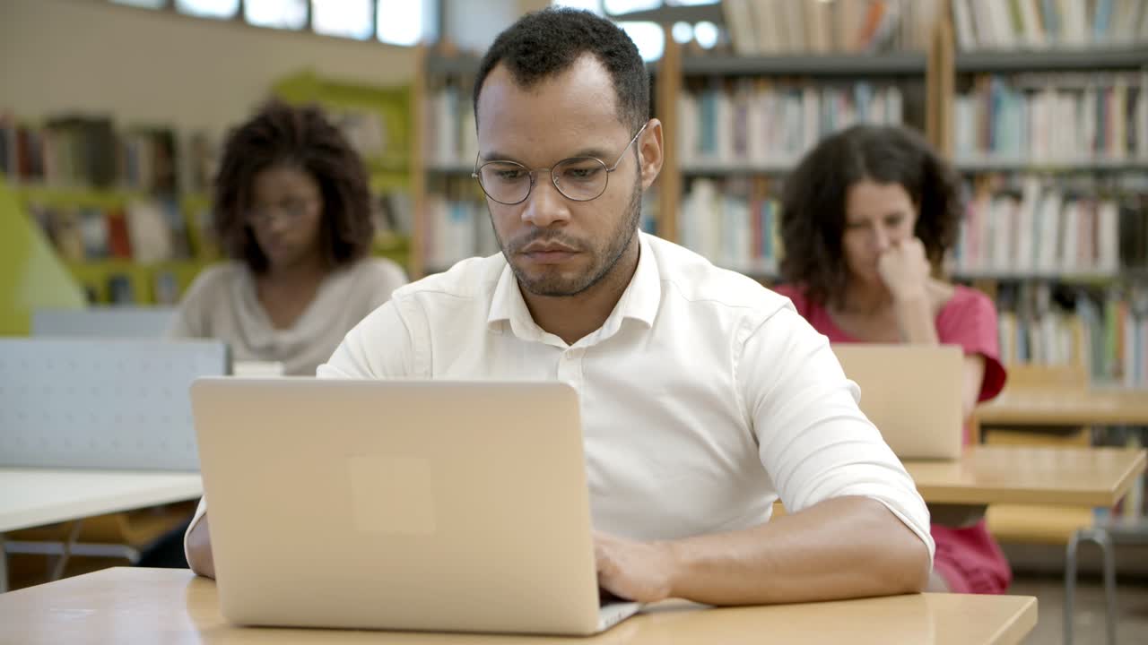 vista frontal del hombre afroamericano enfocado usando una computadora portátil en la biblioteca