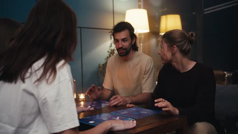 four friends play a board game sitting on the sofa in the evening in a cozy home. video filmed in high quality