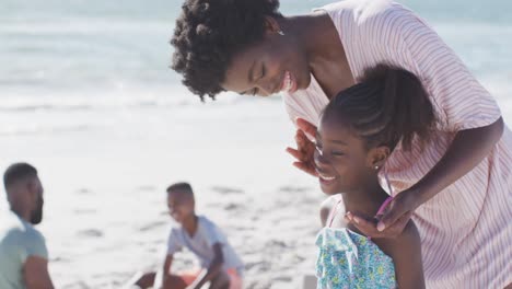 Video-Einer-Glücklichen-Afroamerikanischen-Mutter,-Die-Ihrer-Tochter-Am-Strand-Sonnencreme-Aufträgt