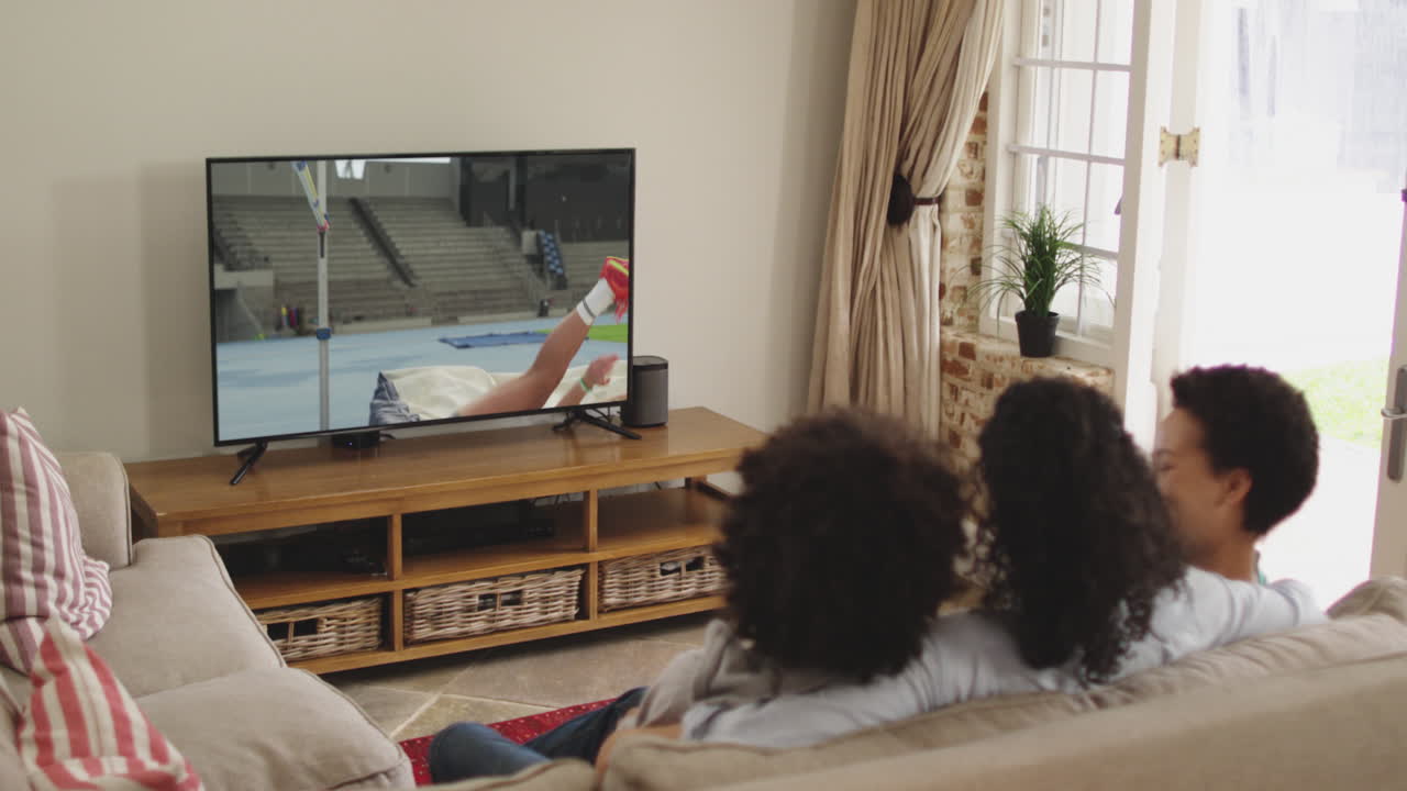 Famiglia felice seduta a casa insieme che guarda l'atletica salto in alto in TV