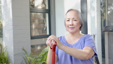 Senior asian woman holding walking cane, sitting outdoors and smiling confidently