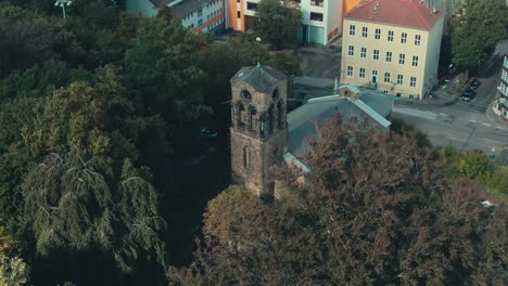 A-historic-church-amidst-lush-trees-in-an-urban-environment,-daylight,-aerial-view