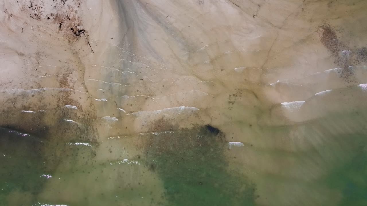 antena: toma estática de arriba hacia abajo del océano y patrones en la arena