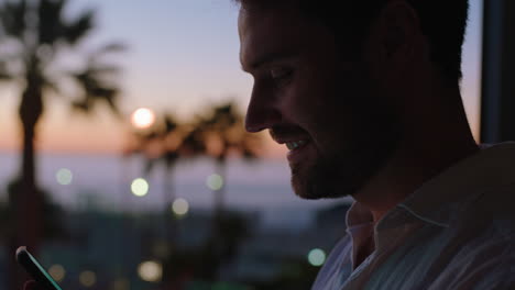 young-man-using-smartphone-in-hotel-room-texting-sharing-vacation-lifestyle-on-social-media-enjoying-view-of-ocean-at-sunset