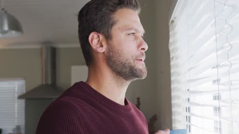 Video-of-thoughtful-caucasian-man-drinking-coffee-and-looking-outside-window