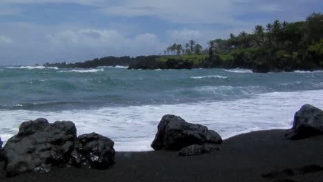 large waves roll into a black sand beach