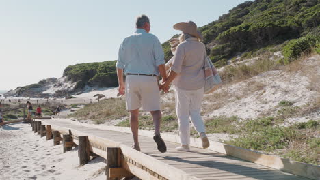 senior couple on summer vacation walking along wooden boardwalk on way to beach