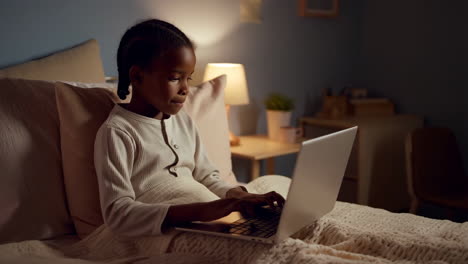 young girl using laptop in bed at night