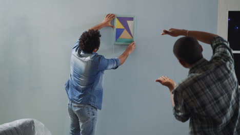 Black-man-helps-colleague-to-hang-drawing-straight-on-wall