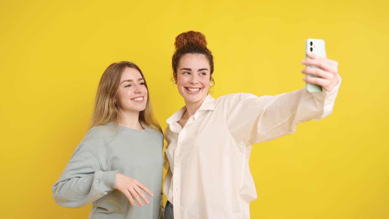 Giovani donne allegre che si scattano selfie su sfondo giallo