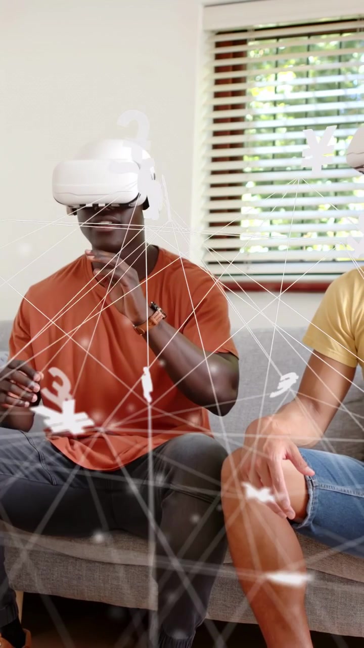 Vertical video: Man adjusting VR and starting finance AR on couch with friend, moving money icons