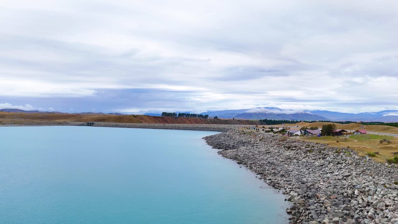 Aerial footage captures Lake Pukaki's turquoise waters and rocky shoreline under overcast skies, showcasing New Zealand's natural beauty