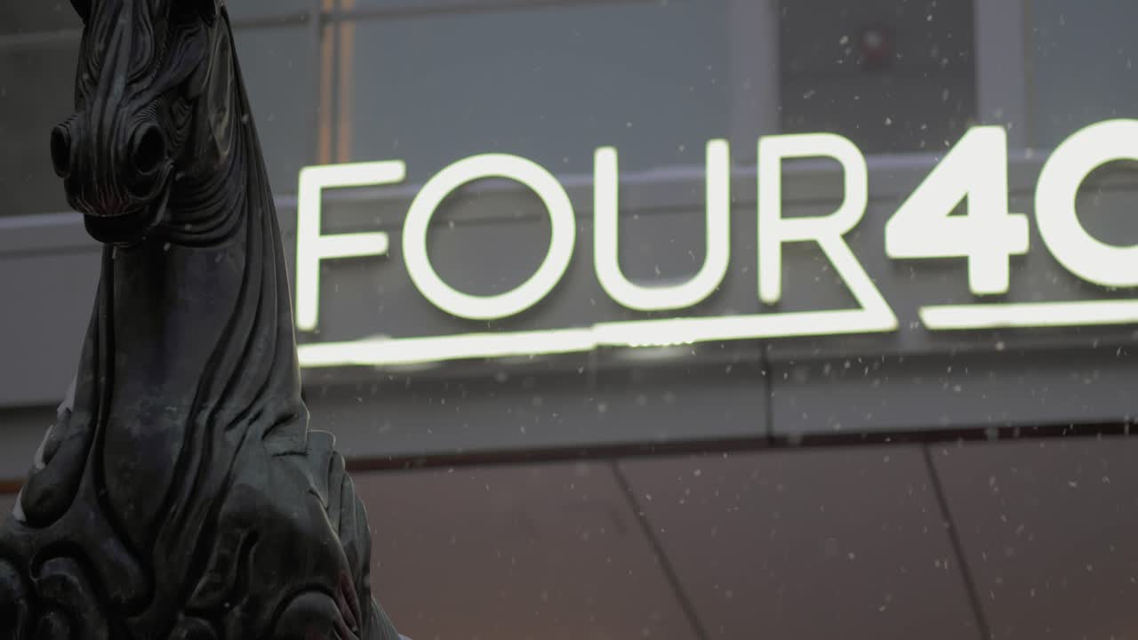Inquadratura statica media di una statua di cavallo in bronzo scuro in primo piano con un cartello luminoso dell'hotel Four Seasons sullo sfondo mentre cade una leggera nevicata nel centro di Chicago