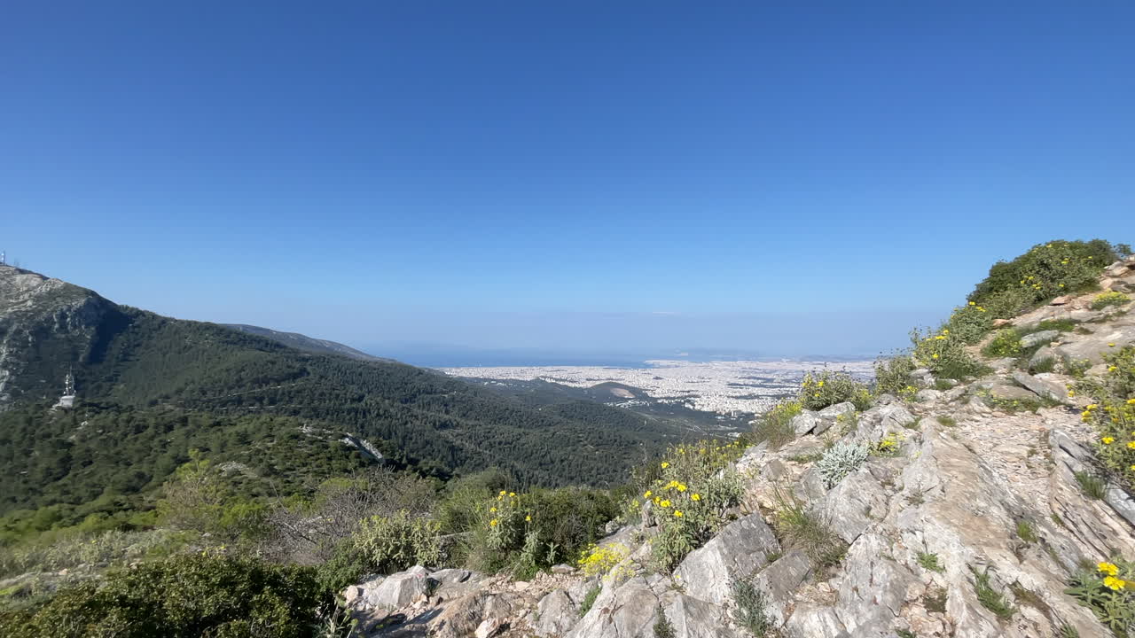 Panoramic shot transitioning from a rock cairn on the Korakovouni summit to the mount Hymettus with city landscape of Athens Attica in the background