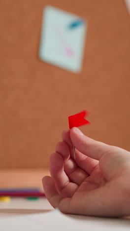 Child spins pin with red flag in hand. Schoolgirl examines stationery device considering educational tasks near big paper notepad and cork board with notes