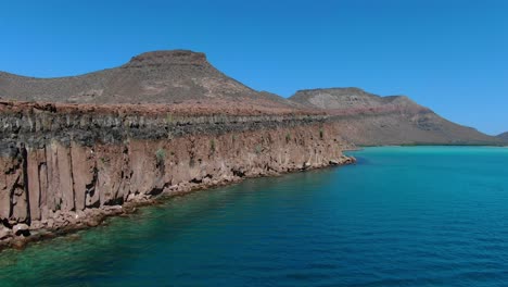 Aerial-view-moving-forward-Ascending-shot,-Scenic-view-tourist-boat-on-the-emerald-green-sea-of-Isla-Espiritu-Santo-in-Baja-Sur-Mexico,-mountain-Hill-in-the-background