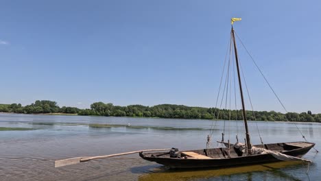 traditional wooden sailing scow floats moored in shallow river current