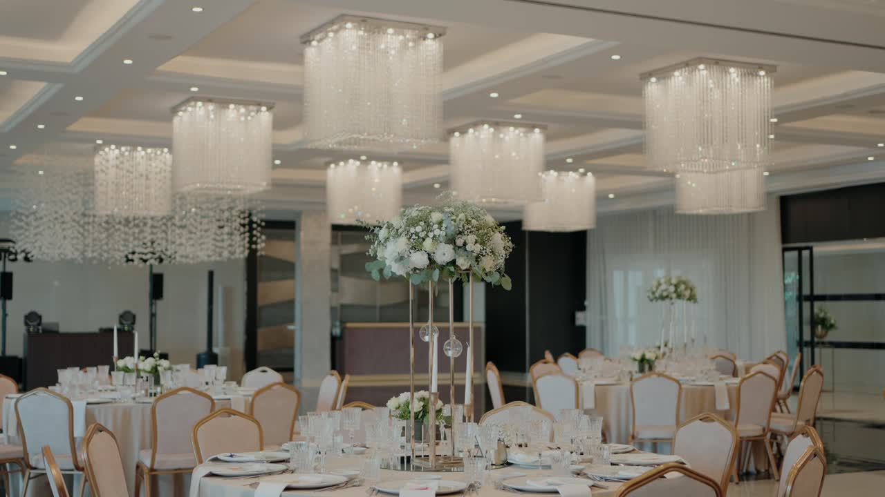 Elegant wedding hall with chandeliers and tables adorned with floral centerpieces