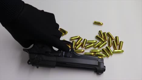 Person-wearing-a-black-glove-picks-up-a-firearm-magazine-and-then-picks-up-the-firearm-leaving-bullets-on-the-table