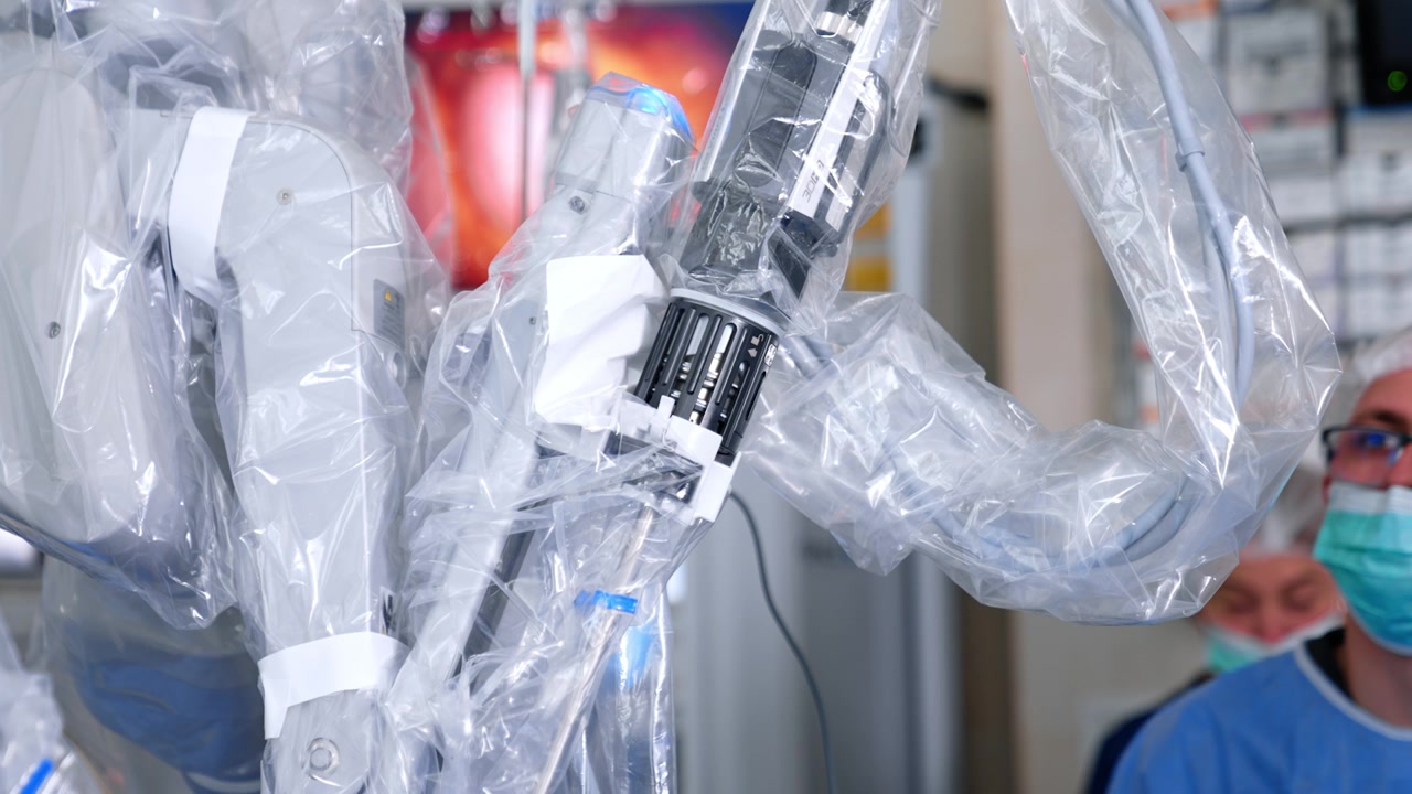 Medico donna non identificato sta di fronte alla moderna macchina Da Vinci in funzione. Il braccio robotico coperto di plastica si muove eseguendo un intervento chirurgico.