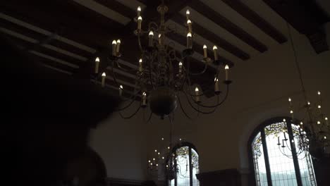 historic chandelier with faux candles hangs in a beautiful old room with large wooden framed windows in the background