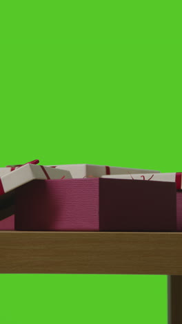 vertical video of man putting present into gift wrapped box on table shot against green screen 2