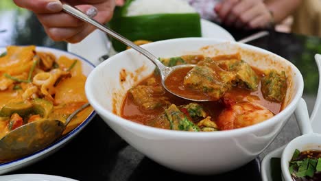 hands serving thai sour soup into plates