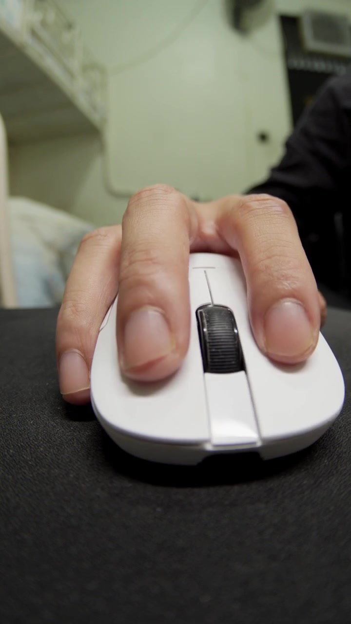 Vertical close-up shot of a person using a white computer mouse on a black mousepad in an office setup in London. Ideal for technology, gaming, office work, and digital business marketing