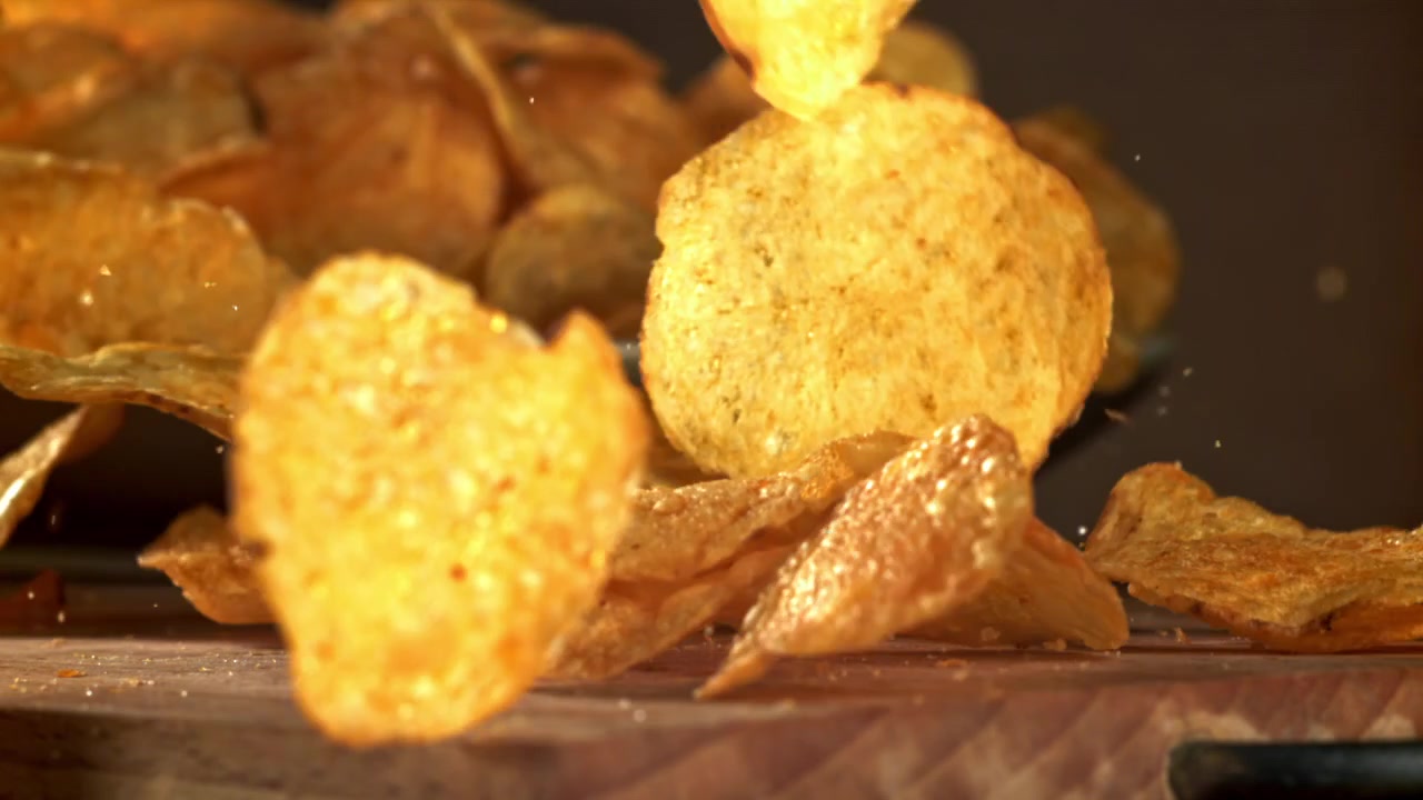 Crispy Potato Chips Falling onto a Wooden Surface in Slow Motion