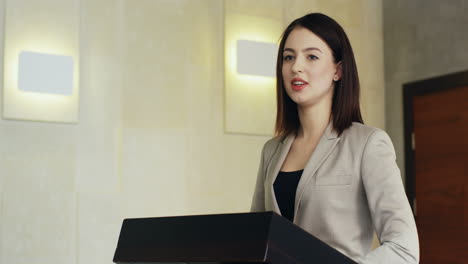 close-up view of caucasian businesswoman speaker on a podium wearing formal clothes and talking in a conference room in front to many people