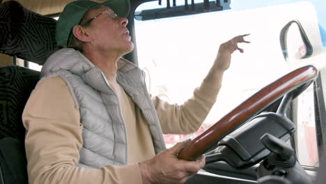 bottom view of older worker wearing cap and vest driving a truck in a logistics park