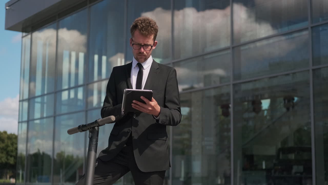 hombre de negocios usando una tableta cerca de un scooter eléctrico fuera de un edificio moderno