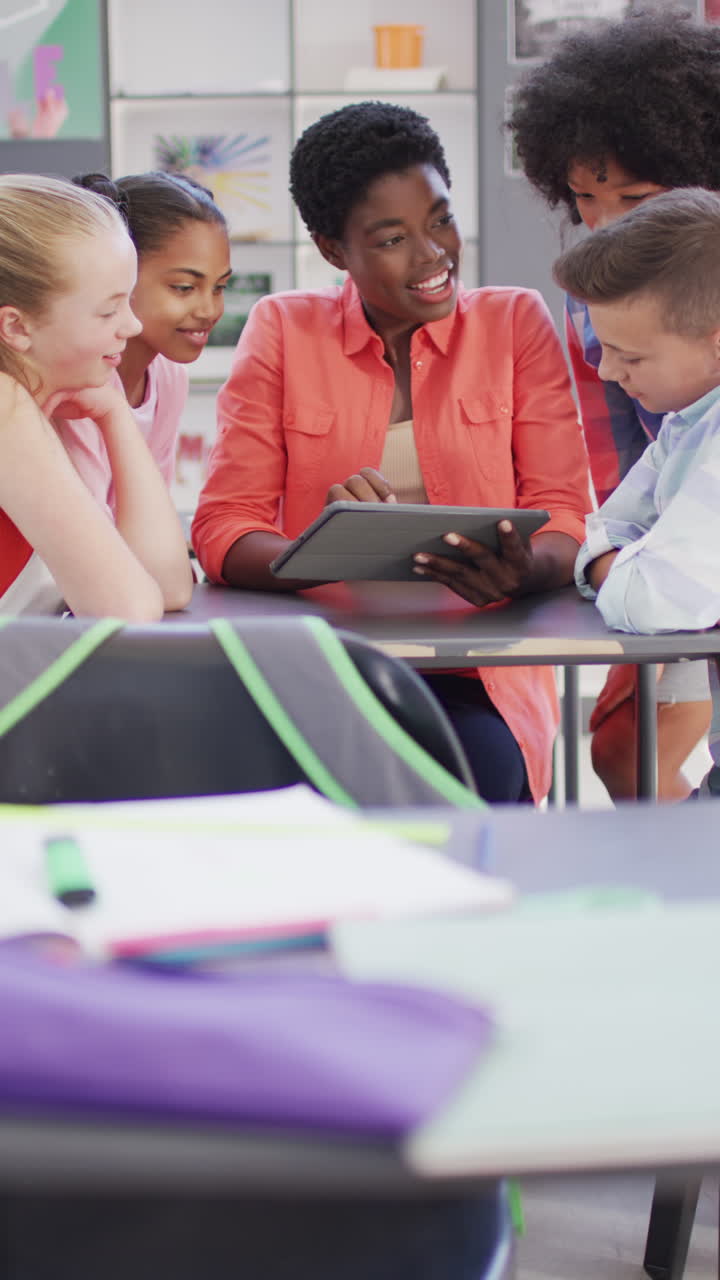 Vertical video of happy diverse female teacher and schoolchildren in school classroom